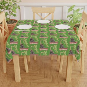 Puede incluir: Un mantel verde con un patrón repetido de árboles bonsái en macetas. El mantel está puesto sobre una mesa de madera con dos sillas.