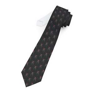 May include: A black tie with a repeating pattern of red and grey spiders. The spiders have red bodies and grey legs, set against a dark background. The tie is folded over a white surface.