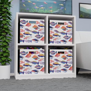 May include: A white four-cube storage organizer unit featuring four fabric storage bins. Each bin is decorated with a repeating pattern of colorful tropical fish in shades of orange, blue, purple, and pink against a white background.