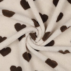 Könnte beinhalten: Cremefarbener Stoff mit einem braunen Herzmuster. Der Stoff ist weich und flauschig, mit einer flauschigen Textur.