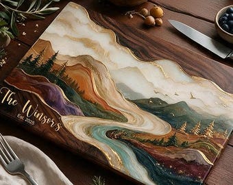 May include: A rectangular wooden serving board featuring a resin art landscape of mountains, a winding river, and pine trees. The board is engraved with the text The Winsors Est. 2025. The resin design incorporates white, gold, blue, and brown tones.