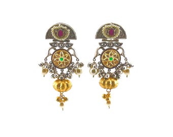 May include: A pair of silver-toned earrings featuring a semi-circular top with a central red stone, a circular middle section with a green stone, and a gold-toned pumpkin-shaped bead at the bottom, accented with small white pearls and silver charms.