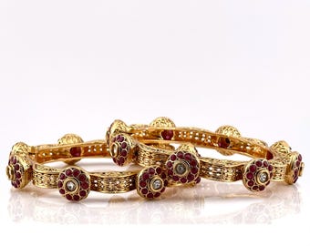 May include: A pair of gold bangles with intricate designs and red and white stones.