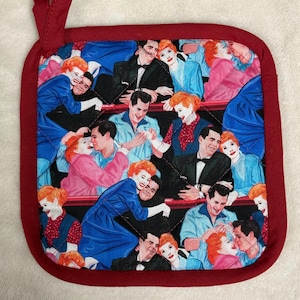 May include: Square quilted pot holder with a burgundy border and hanging loop. The center features a repeating pattern of a vintage couple embracing. The fabric has a black background with the couples in various outfits.