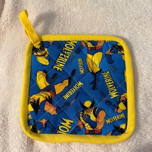 May include: Square blue and yellow Wolverine-themed pot holder. The pot holder features a repeating pattern of the Wolverine character in yellow and blue, with the word "Wolverine" printed on the fabric. The edges are trimmed with yellow fabric and a yellow loop.