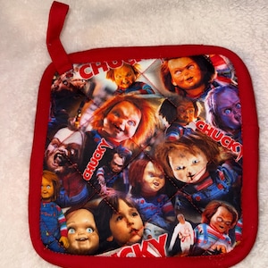 Puede incluir: Un agarrador de cocina cuadrado y acolchado con un borde de tela roja y una presilla para colgar. La superficie presenta un collage repetitivo del personaje Chucky de la franquicia de terror Child's Play, incluyendo la muñeca pelirroja y el texto CHUCKY.