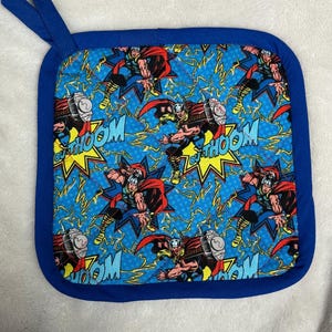 May include: Square blue pot holder with a blue loop for hanging. The pot holder features a repeating comic book design of Thor, with the word "WHOOM" in yellow starbursts on a blue background. The edges are trimmed in blue.