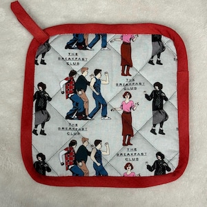 Puede incluir: Salvamanteles cuadrado y acolchado con borde rojo y lazo para colgar. La tela principal es gris claro con un patrón repetido de personajes de la película "The Breakfast Club". El texto "THE BREAKFAST CLUB" también está impreso.