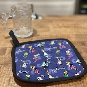 May include: A blue quilted hot pad with a black border. The hot pad features a repeating pattern of the Jetsons characters and the word "Jetsons".