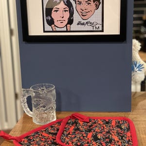 May include: Two red and black pot holders with a pattern of a comic book character. The pot holders have a red border and are made of fabric.