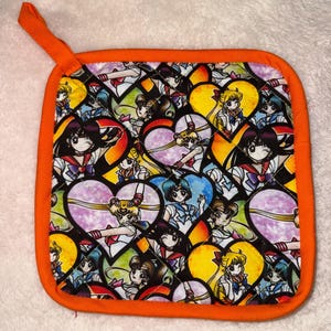 Könnte beinhalten: Quadratischer, gesteppter Topflappen mit orangefarbenem Rand und Aufhängeschlaufe. Der Stoff zeigt ein sich wiederholendes Muster von Anime-Charakteren in herzförmigen Rahmen in Rot-, Blau-, Gelb- und Lilatönen.