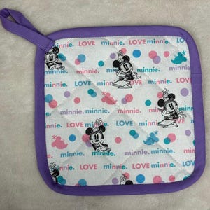 May include: Square quilted pot holder with a purple border and hanging loop. The white fabric is patterned with Minnie Mouse illustrations, polka dots, and the words "LOVE minnie."