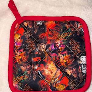 May include: A square quilted pot holder with a red fabric border and a matching red hanging loop. The central fabric features a repeating graphic print of the horror character Freddy Krueger in various poses, set against a fiery orange and black background.