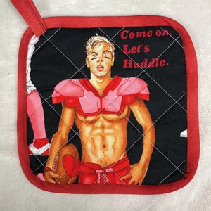 May include: Square red and black pot holder with a football player illustration. The illustration features a muscular figure in red football gear holding a football. Text on the pot holder reads "Come on. Let's Huddle."
