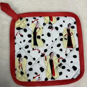 Puede incluir: Salvamanteles cuadrado con estampado de lunares blancos y negros, borde rojo y lazo rojo. El diseño presenta una imagen de dibujos animados de una mujer con un vestido negro y un abrigo color crema.