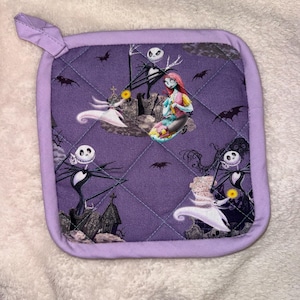 May include: A square quilted pot holder with a purple background featuring a repeating pattern of characters from The Nightmare Before Christmas, including Jack Skellington, Sally, and Zero the ghost dog, surrounded by tombstones and bats.