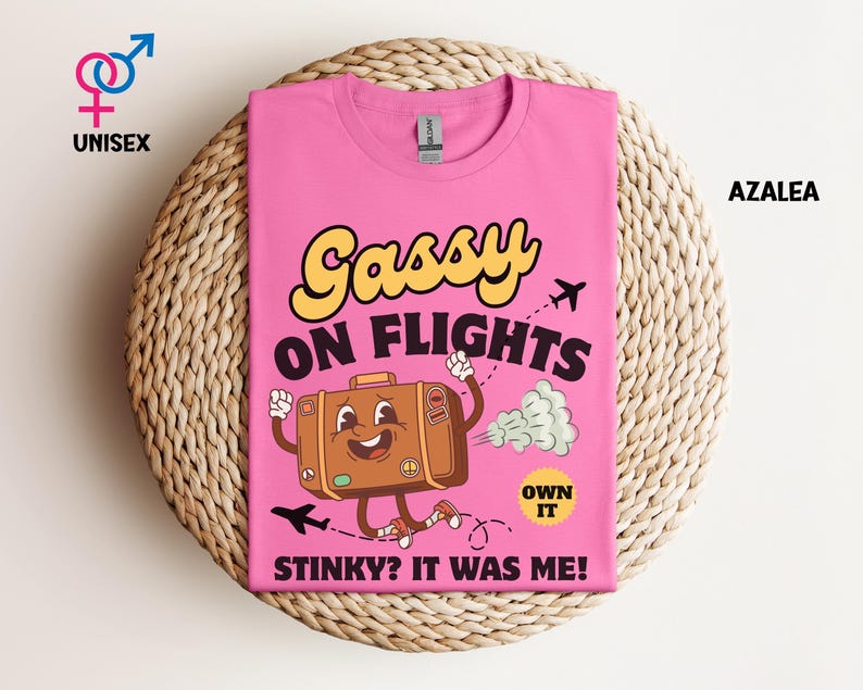 May include: Pink unisex t-shirt with the text "Gassy on Flights" and a cartoon suitcase character. The suitcase is brown with a smiling face and running legs. The shirt also has the text "Stinky? It was me!" and "Own it".