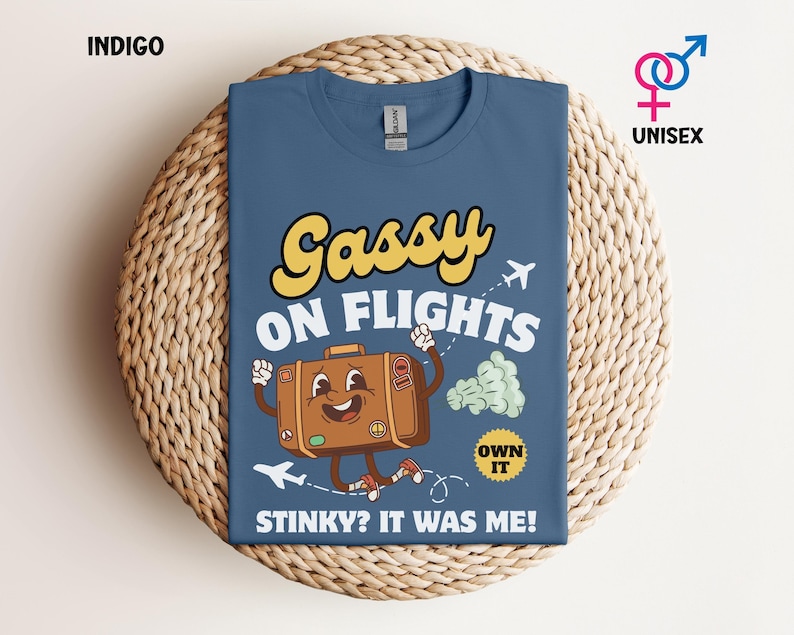 May include: Indigo blue unisex t-shirt with the text "Gassy on Flights" in yellow and white. A cartoon suitcase with arms and legs is featured in the design, along with airplane graphics and the phrase "Stinky? It was me!"