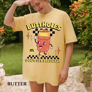 May include: Butter-colored t-shirt with the text "BUTTHOLES" in yellow and black. The shirt features a cartoon illustration of a jar with a face and the words "BUTT FACTS DON'T GET PREGNANT".