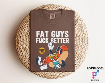 May include: Espresso-colored t-shirt with the text "FAT GUYS FUCK BETTER" in white. A cartoon hot dog with a drink is featured below the text. The shirt is unisex.