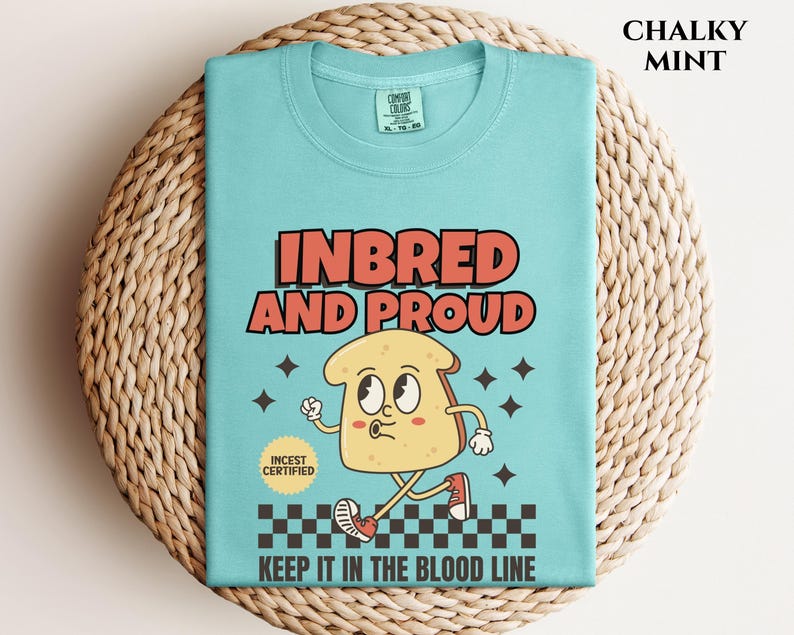 May include: A light blue t-shirt with a cartoon illustration of a slice of bread with a face. The text "Inbred and Proud" is printed in red and white. The text "Keep it in the blood line" is printed in black. The text "Incest Certified" is printed in a circle with a red border.