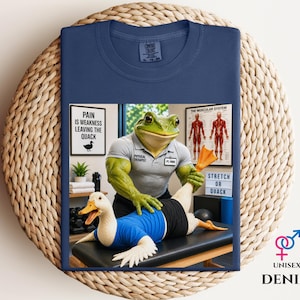 May include: Navy blue t-shirt with a comical design of a frog physiotherapist treating a duck. The frog is wearing a gray shirt with the words "Physical Therapist". The duck is wearing a blue shirt. The text on the shirt says "Stretch or Quack".