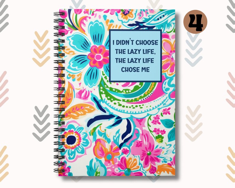 May include: A spiral bound notebook with a white background and a colorful floral pattern. The notebook has a blue cover with the text "I didn't choose the lazy life, the lazy life chose me".