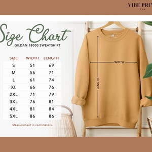 May include: Size chart for a Gildan 18000 sweatshirt, showing measurements in inches for width and length for sizes S through 5XL. The chart is displayed next to a tan sweatshirt.