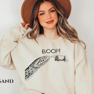 May include: A cream colored sweatshirt with a black snake and the text "BOOP!" printed on the front.