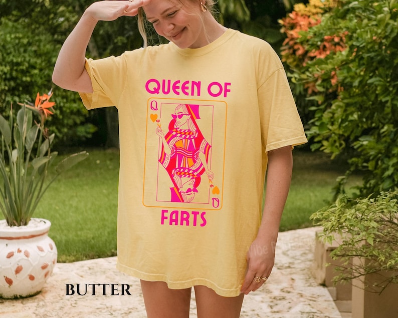 May include: A yellow t-shirt with a graphic of a playing card featuring a queen wearing sunglasses. The text "QUEEN OF FARTS" is printed in pink. The word "BUTTER" is printed at the bottom of the shirt.
