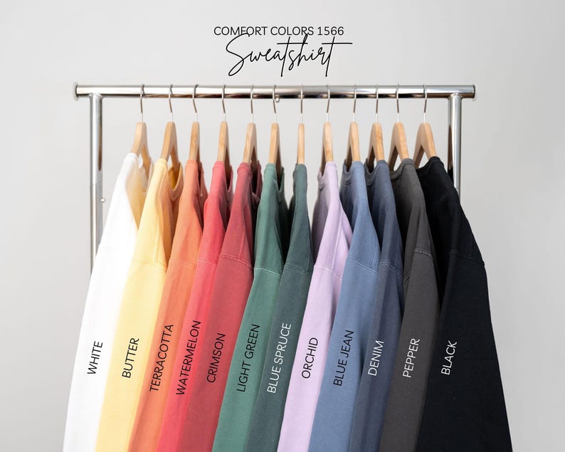 May include: A rack of Comfort Colors 1566 sweatshirts in various colors, including white, butter, terracotta, watermelon, crimson, light green, blue spruce, orchid, blue jean, denim, pepper, and black. The word "Sweatshirt" is written above the shirts.