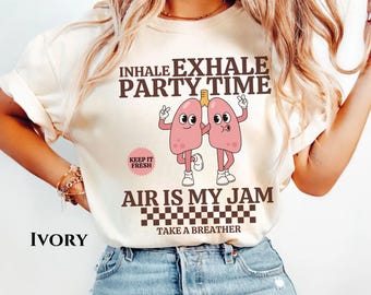 May include: Ivory t-shirt with a graphic of two cartoon lungs with the text "INHALE EXHALE PARTY TIME" and "AIR IS MY JAM" with a checkered pattern and the text "TAKE A BREATHER".