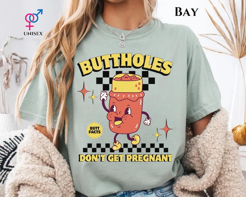 May include: A light green unisex t-shirt with the text "BUTTHOLES DON'T GET PREGNANT" in yellow and black. The shirt features a cartoon illustration of a jar with a face and arms.