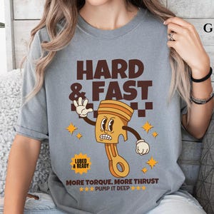 Puede incluir: Camiseta gris con una ilustraci&oacute;n de dibujos animados de un pist&oacute;n con el texto "HARD & FAST", "LUBED & READY", "MORE TORQUE, MORE THRUST" y "***PUMP IT DEEP***".