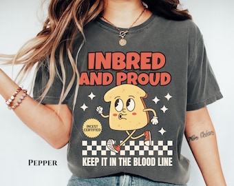 May include: A gray t-shirt with the text "INBRED AND PROUD" in red and white. A cartoon illustration of a slice of bread with a face and legs is walking on a checkered pattern. The text "INCEST CERTIFIED" is in a circle above the bread. The text "KEEP IT IN THE BLOOD LINE" is below the bread.