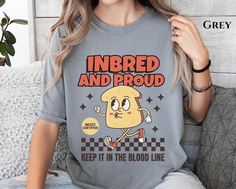 May include: A grey t-shirt with a cartoon illustration of a slice of bread with a face. The text "Inbred and Proud" is above the bread and "Keep it in the blood line" is below the bread. There is a small square with the text "Incest Certified" next to the bread.
