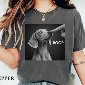 May include: Dark grey t-shirt featuring a black and white image of a dog being booped on the nose. The word "BOOP" is printed in white. The word "PEPPER" is printed in black at the bottom of the shirt.
