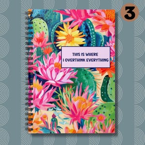 May include: A spiral bound notebook with a colorful floral design featuring pink, yellow, green, and blue flowers. The text "This is where I overthink everything" is printed on a purple rectangle on the front cover.