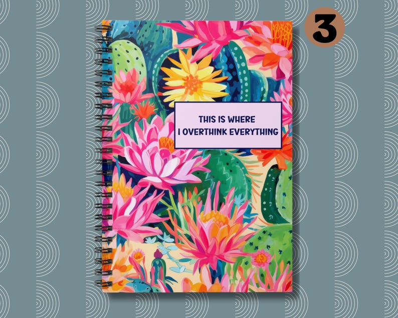 May include: A spiral bound notebook with a colorful floral design featuring pink, yellow, green, and blue flowers. The text "This is where I overthink everything" is printed on a purple rectangle on the front cover.