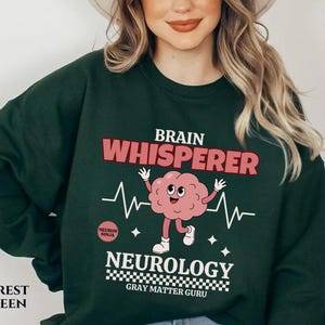 May include: Forest green sweatshirt with a brain graphic and the text "Brain Whisperer Neurology Gray Matter Guru".