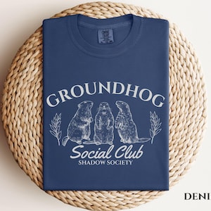 May include: A navy blue t-shirt with a white graphic of three groundhogs and the text "Groundhog Social Club Shadow Society".