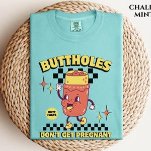 May include: A Chalky Mint colored t-shirt with the words "BUTTHOLES DON'T GET PREGNANT" and a cartoon illustration of a smiling jar with a yellow lid. The shirt also has the words "BUTT FACTS".