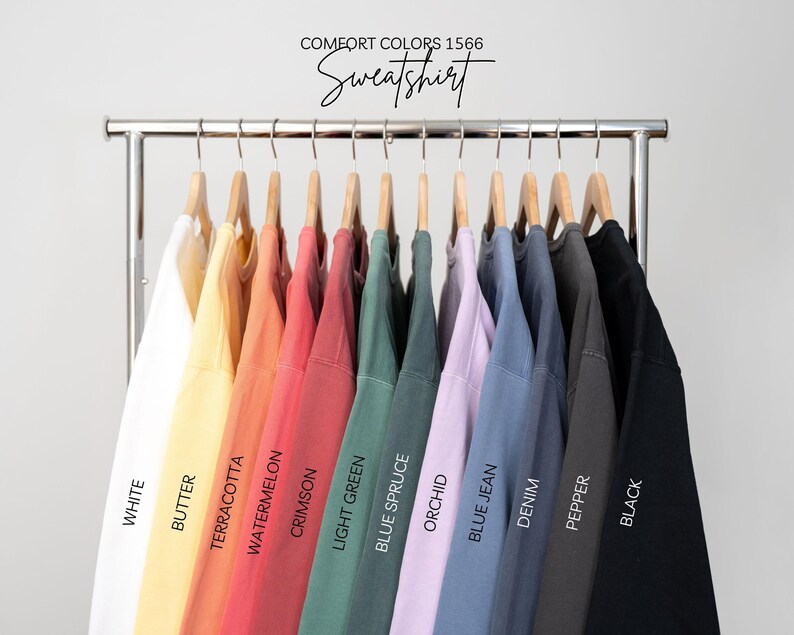 May include: A rack of Comfort Colors 1566 sweatshirts in various colors, including white, butter, terracotta, watermelon, crimson, light green, blue spruce, orchid, blue jean, denim, pepper, and black. The word "Sweatshirt" is written above the shirts.