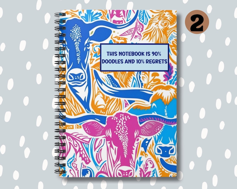 May include: A spiral bound notebook with a colorful design featuring a repeating pattern of stylized cows and floral elements. The cover has the text "This notebook is 90% doodles and 10% regrets".
