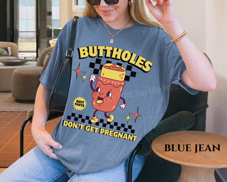 May include: Blue jean-colored t-shirt with a retro-style graphic. The graphic features the word "BUTTHOLES" above a cartoon illustration of a jar with a face, and the text "DON'T GET PREGNANT" below.