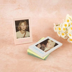 May include: Two small photo frames, one light pink and one white, each with a picture of a woman. The pink frame has "Happy Birthday" written on it. The other frame has "5 years K & P". A bouquet of white daisies is in the background.