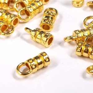 May include: A group of gold-toned metal end caps with a loop on one end and a decorative pattern. The end caps are scattered on a white surface.