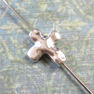 May include: A silver cross charm with a textured surface. The charm is threaded on a silver wire.