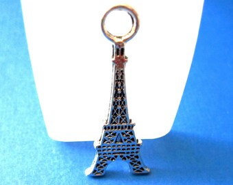May include: Silver charm shaped like the Eiffel Tower with a loop at the top for attaching to a necklace or bracelet.