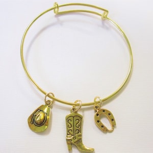 May include: A gold bangle bracelet with three charms: a cowboy hat, a cowboy boot, and a horseshoe.